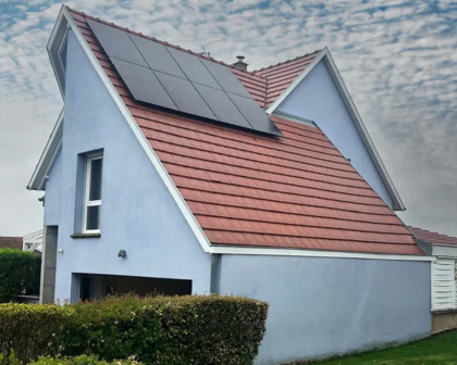 Maison avec panneaux solaires noirs installés sur la toiture inclinée, sous un ciel nuageux.