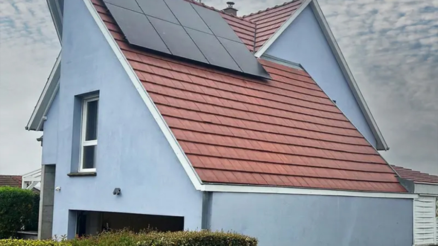 Maison avec panneaux solaires noirs installés sur la toiture inclinée, sous un ciel nuageux.